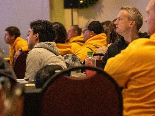 A group of people in yellow shirts are sitting at tables in a conference room.