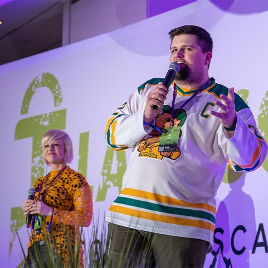 A man holding a microphone with the letter c on his shirt
