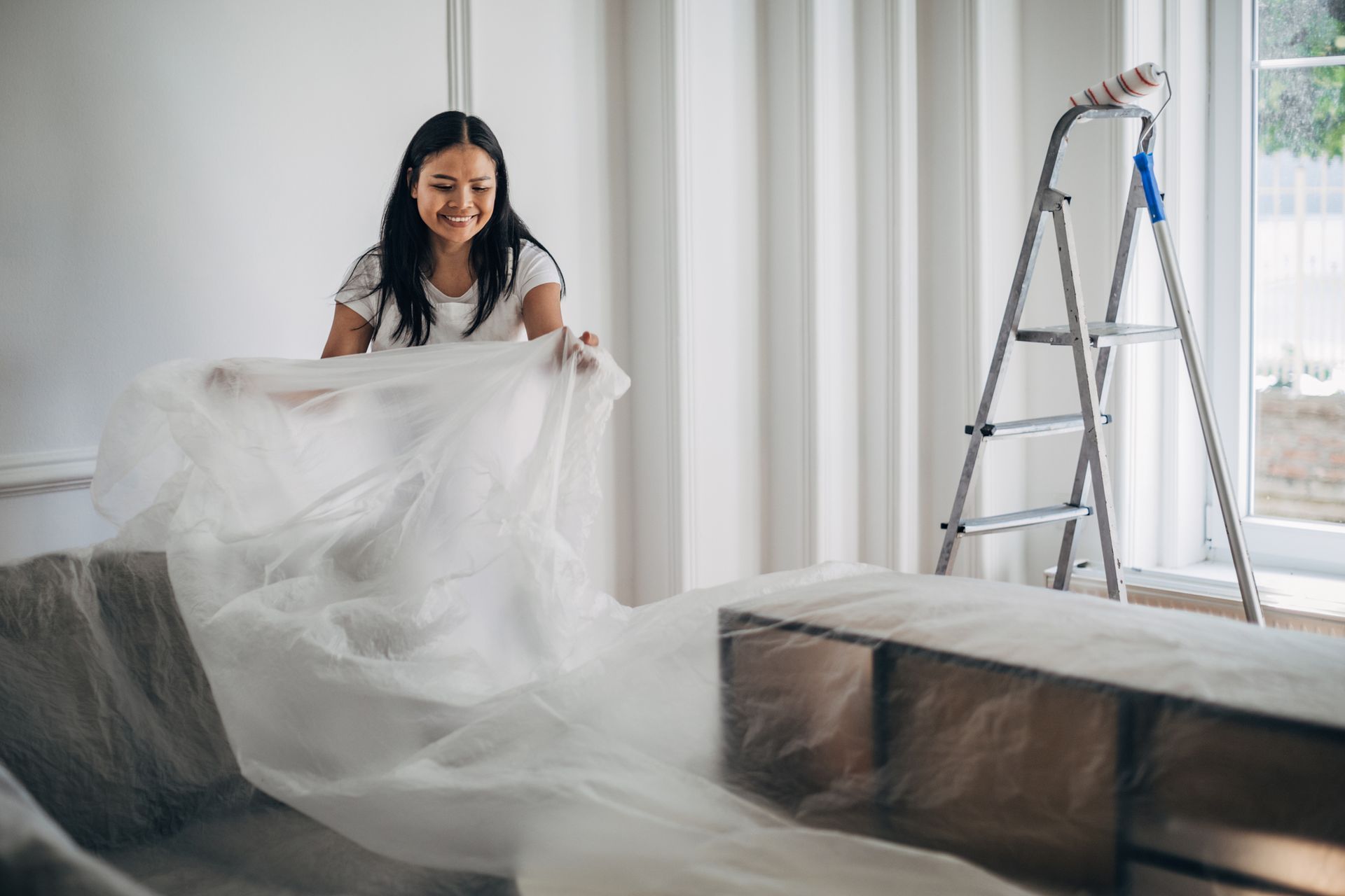 A woman is covering her furniture before the painting of her living room. A woman is covering her furniture before the painting of her living room.