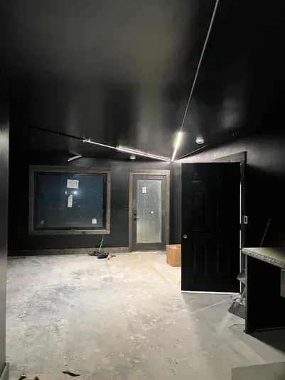 A room painted black with a window, door, and unfinished concrete floor.