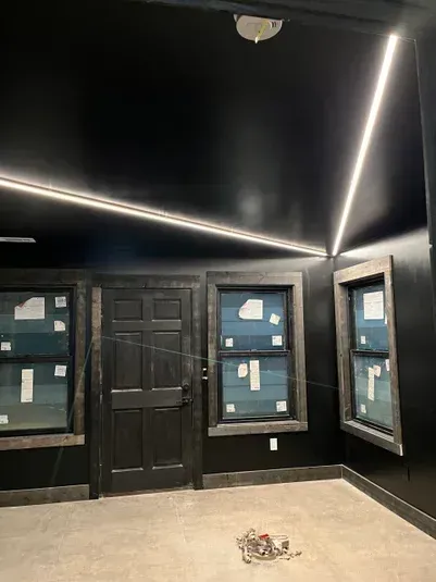 Black room with linear LED lighting, dark door and windows, unfinished construction.