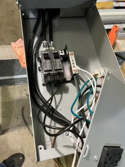 Open electrical panel with black cables, breakers, and wires. Green, white, and black wires visible.