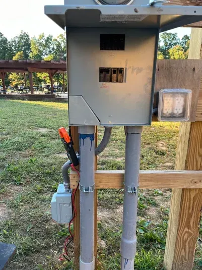 Gray electrical box with conduit, mounted on wooden post, at campsite.