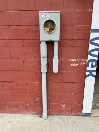 Electrical meter box with gray conduit on a red brick wall.