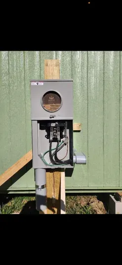 An electrical meter box mounted on a wooden post, with wires visible.