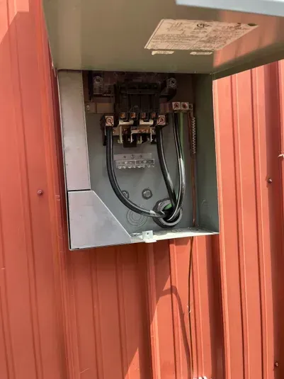 Metal electrical box on a red building, open to reveal black wires and components.