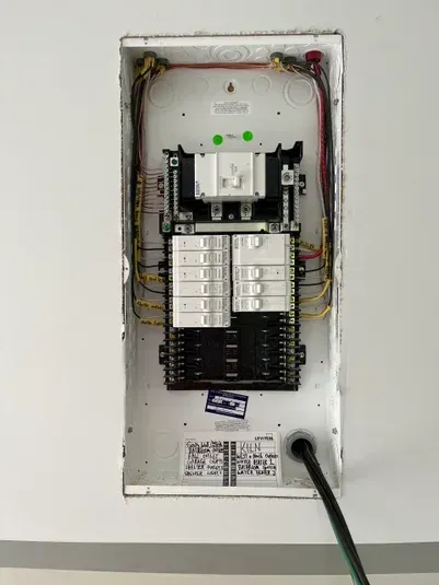 Electrical panel with circuit breakers inside a white wall cutout.