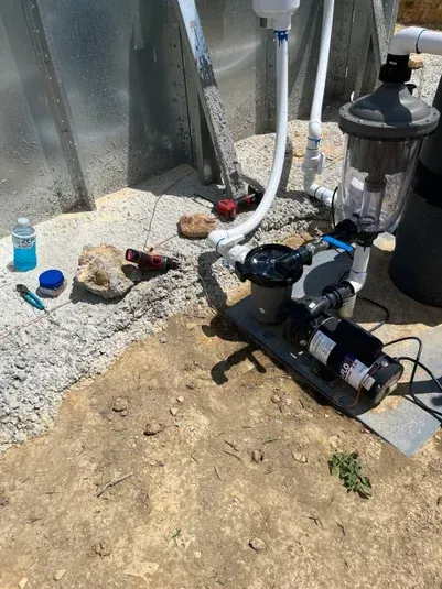 Equipment for pool filtration set up outdoors near a concrete wall; includes pipes, pump, filter, and tools.