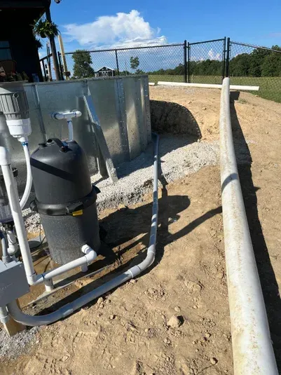 Pool equipment with filtration system, white PVC pipes, and dirt ground.