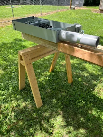 Metal electrical box on a wooden sawhorse outside on grass.