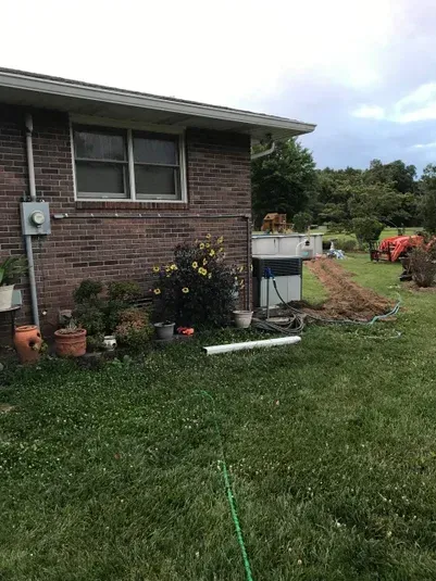 Brick house with a small garden in the yard. Green grass and cloudy sky.