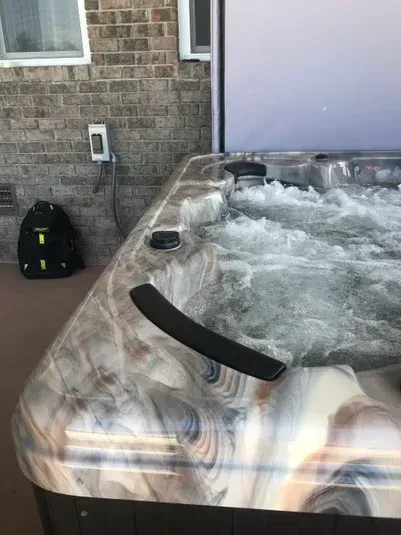 Hot tub with jets, on a patio, next to brick wall and a backpack.