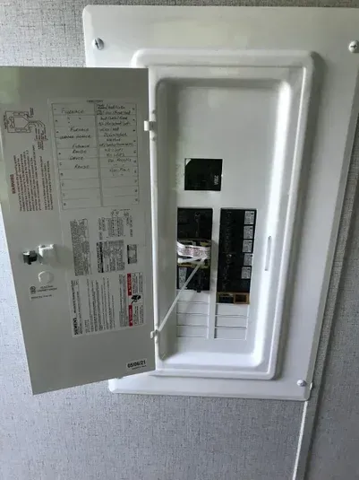 White electrical breaker box with the door open, showing circuit breakers and labeling.
