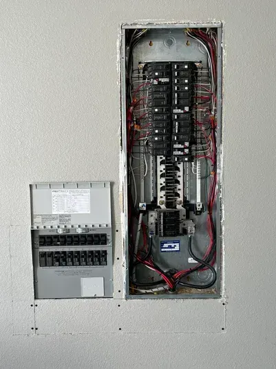 Electrical panel inside wall cavity, showing circuit breakers and wiring.