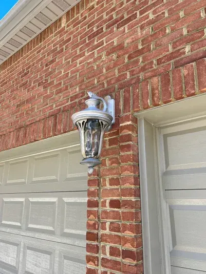 Brick wall with a silver outdoor light fixture next to a white garage door.