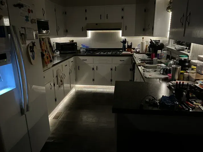 Brightly lit kitchen with white cabinets, black counters, and under-cabinet lighting.