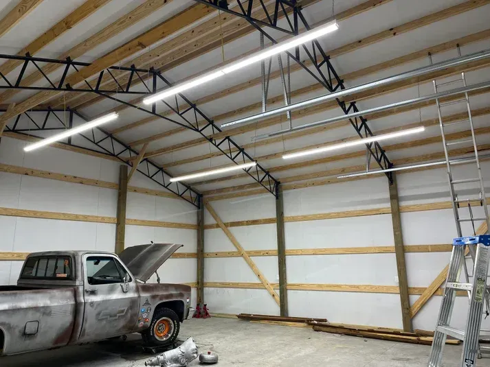 Inside a spacious garage: a classic pickup, overhead lights, and construction.
