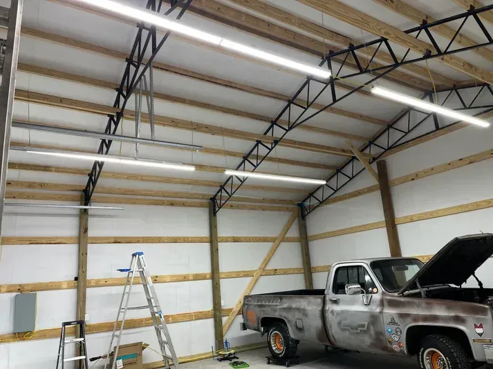 Interior view of a garage with a classic truck, construction materials, and overhead lighting.