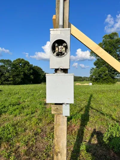 Gray electrical box and meter on a wooden pole in a grassy field with blue sky.