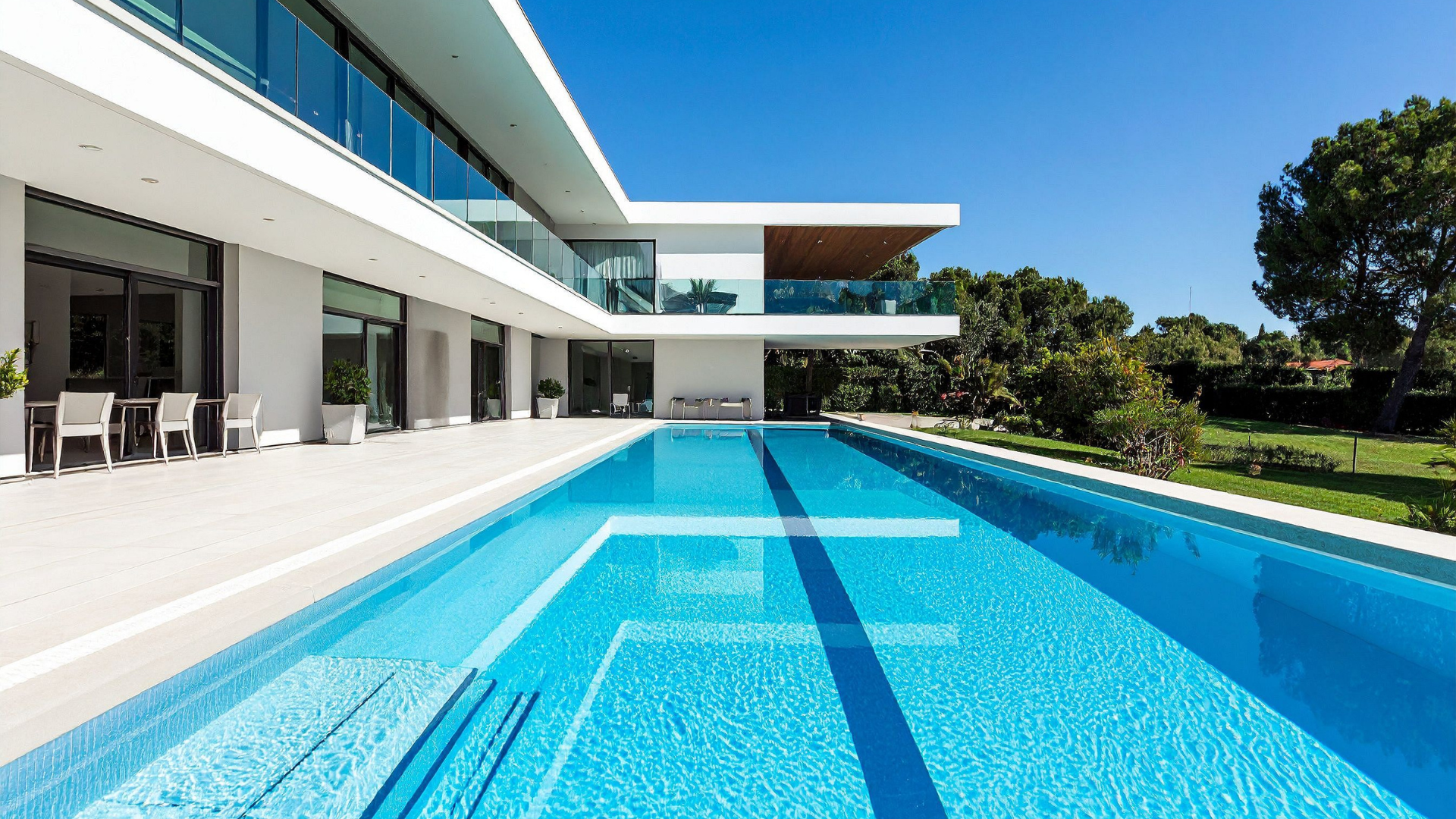Modern white house with a long, blue pool on a sunny day.
