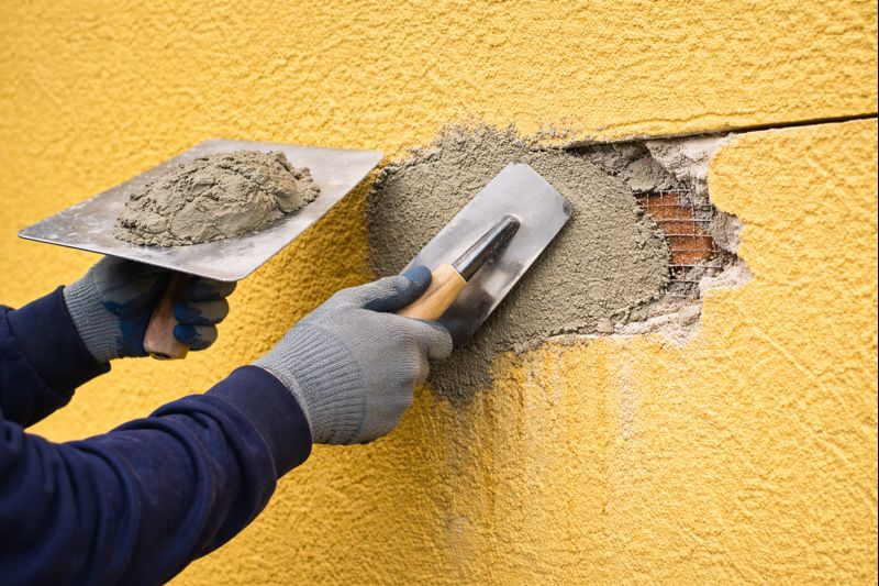 Contractor applying fresh stucco patch to repair damaged exterior wall.