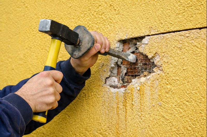 Contractor removing damaged stucco to prepare wall for repair.