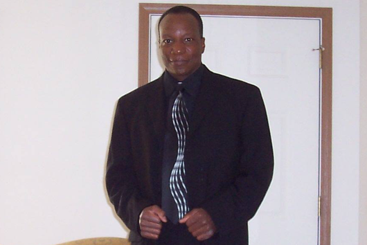 Man in a black suit and tie standing in front of a door.