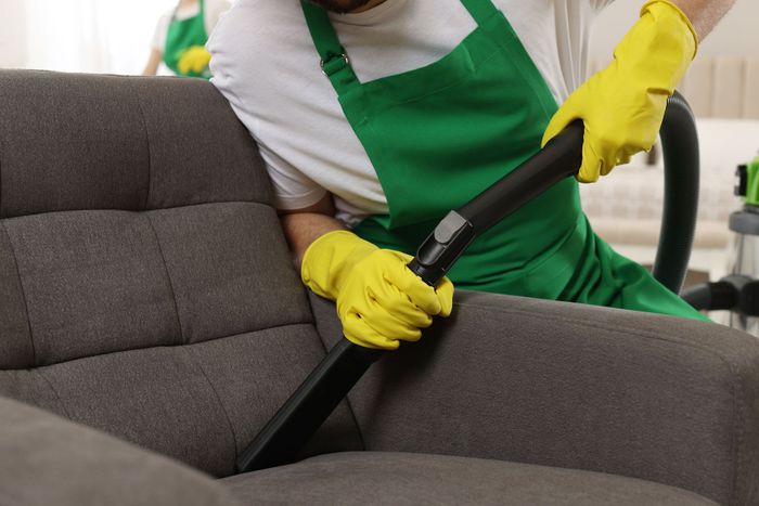 a man wearing yellow gloves is cleaning a couch with a vacuum cleaner