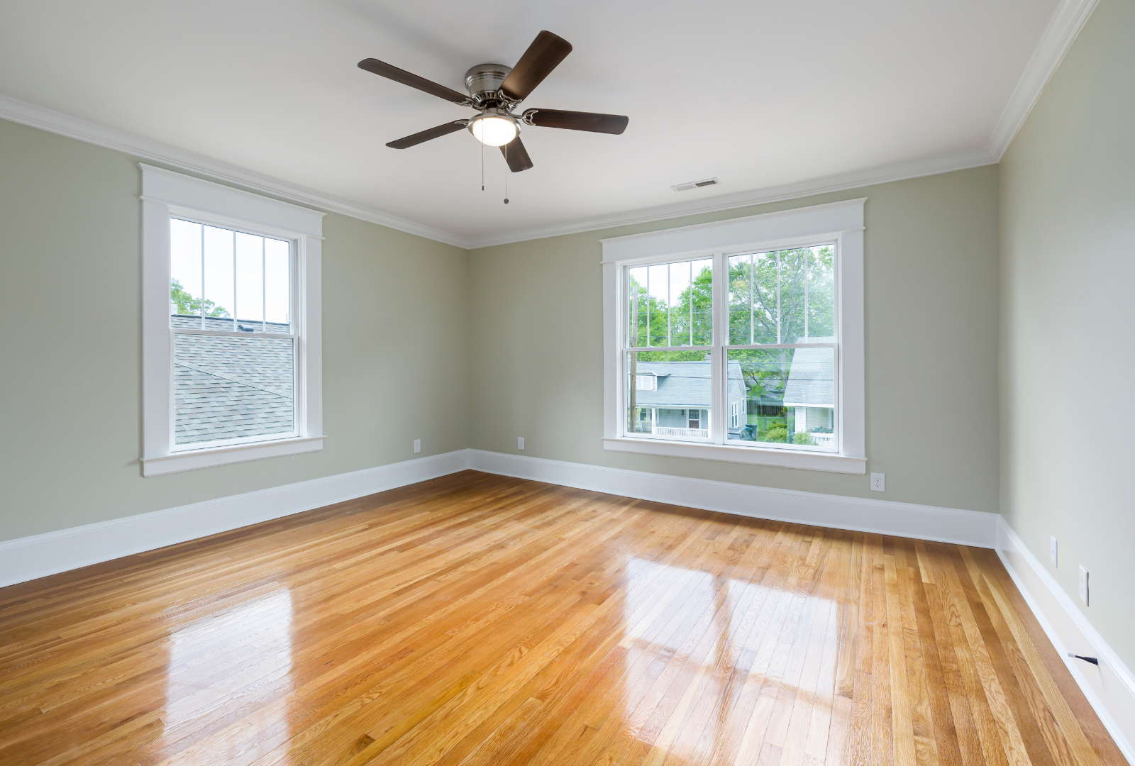 Empty room with light sage green walls, white trim, polished hardwood floors, and a ceiling fan.