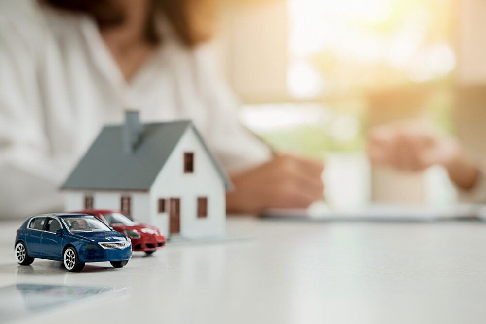 A Woman is Sitting at a Table With a Model House and Two Toy Cars — Key2 Conveyancing In Diamond Beach, NSW