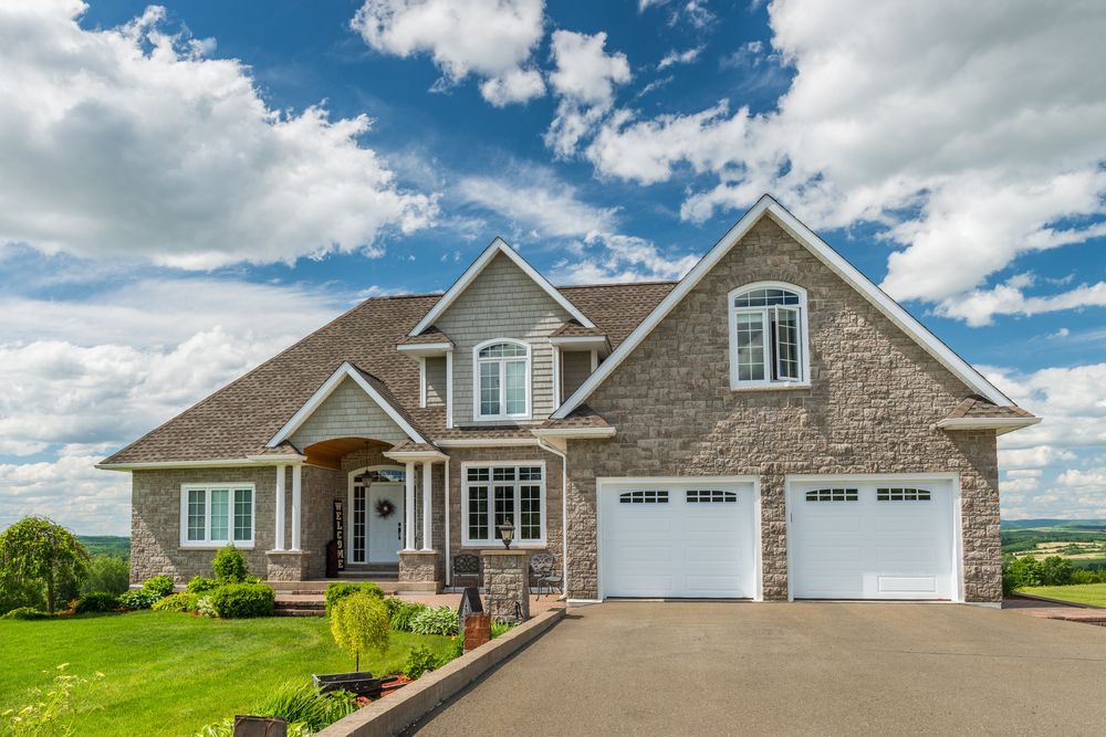 A Large Stone House With Two White Garage Doors on a Sunny Day — Key2 Conveyancing In Diamond Beach, NSW