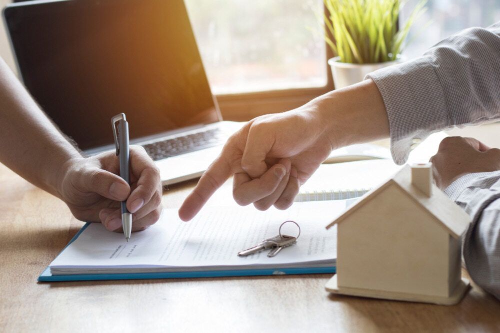 A Person is Pointing at a Model House While Another Person Signs a Document — Key2 Conveyancing In Diamond Beach, NSW