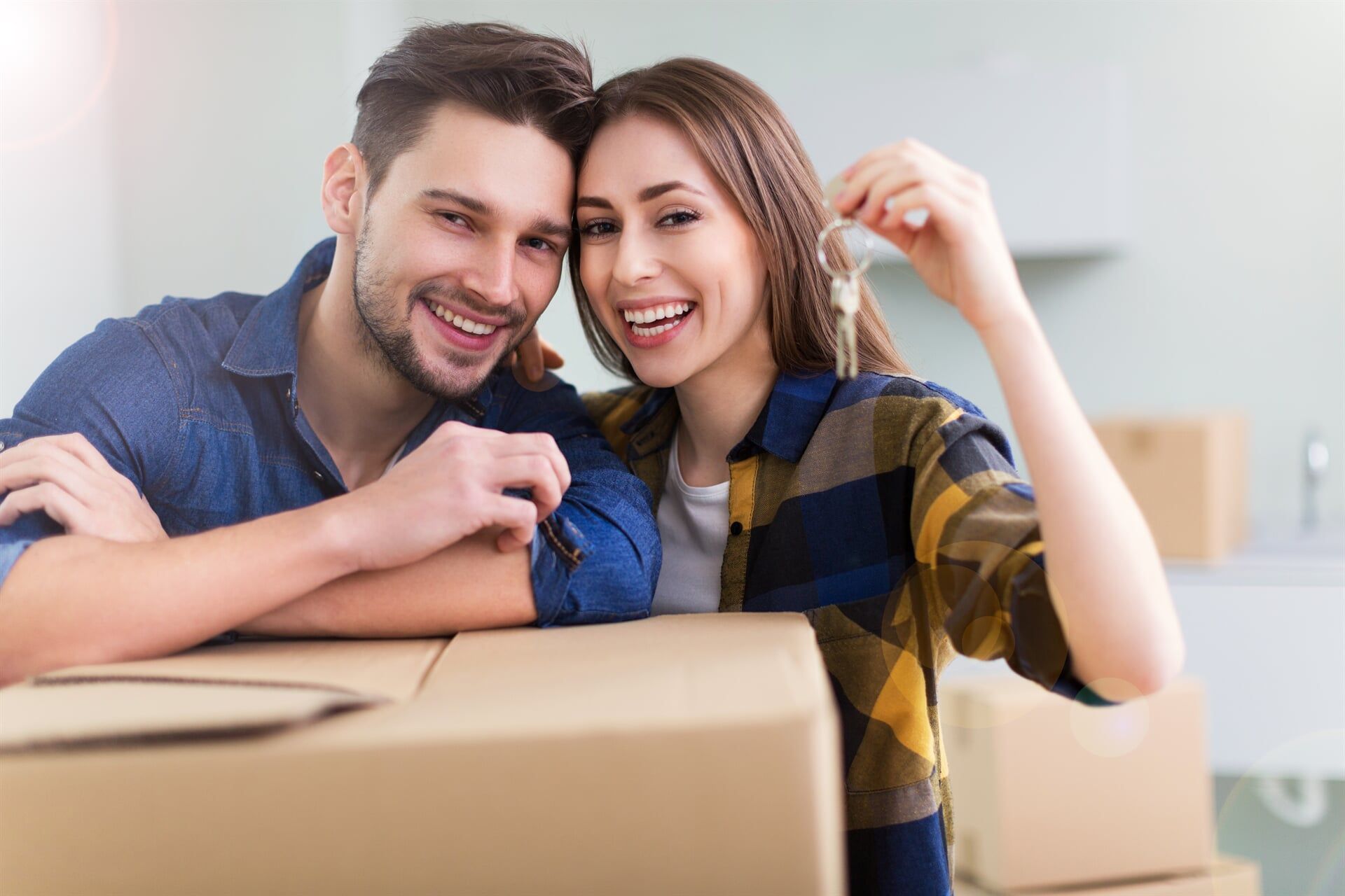 A Man and a Woman Are Sitting on a Cardboard Box Holding Keys to Their New Home — Key2 Conveyancing In Forster, NSW