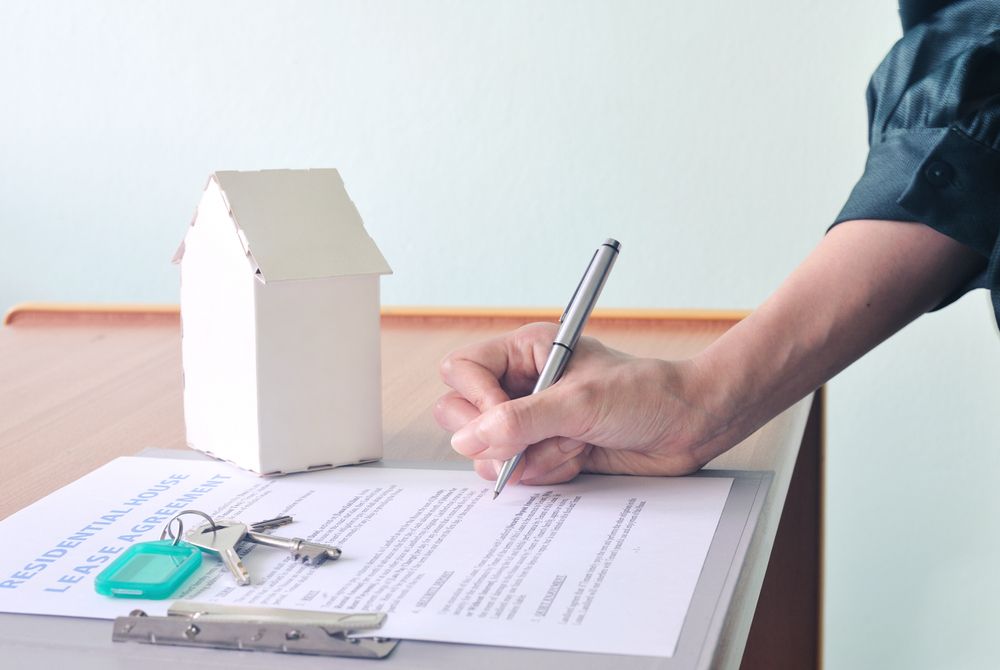 A Person is Writing on a Piece of Paper Next to a Model House and Keys — Key2 Conveyancing In Mid North Coast, NSW