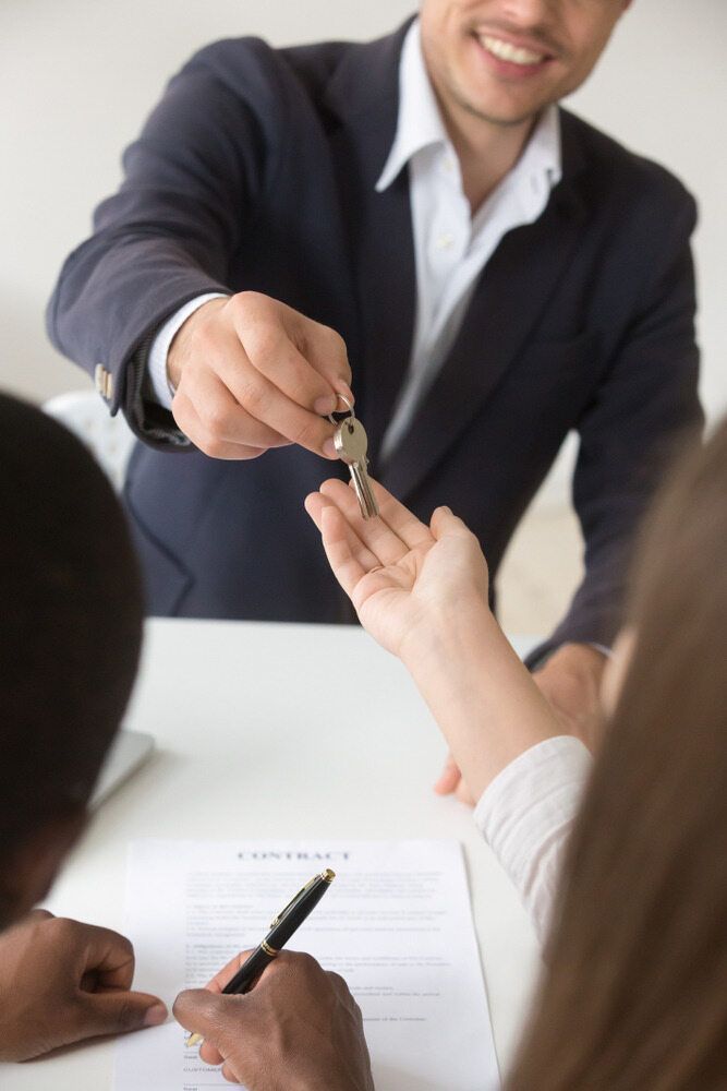 A Man is Giving a Key to a Woman Who is Signing a Contract — Key2 Conveyancing In Pacific Palms, NSW