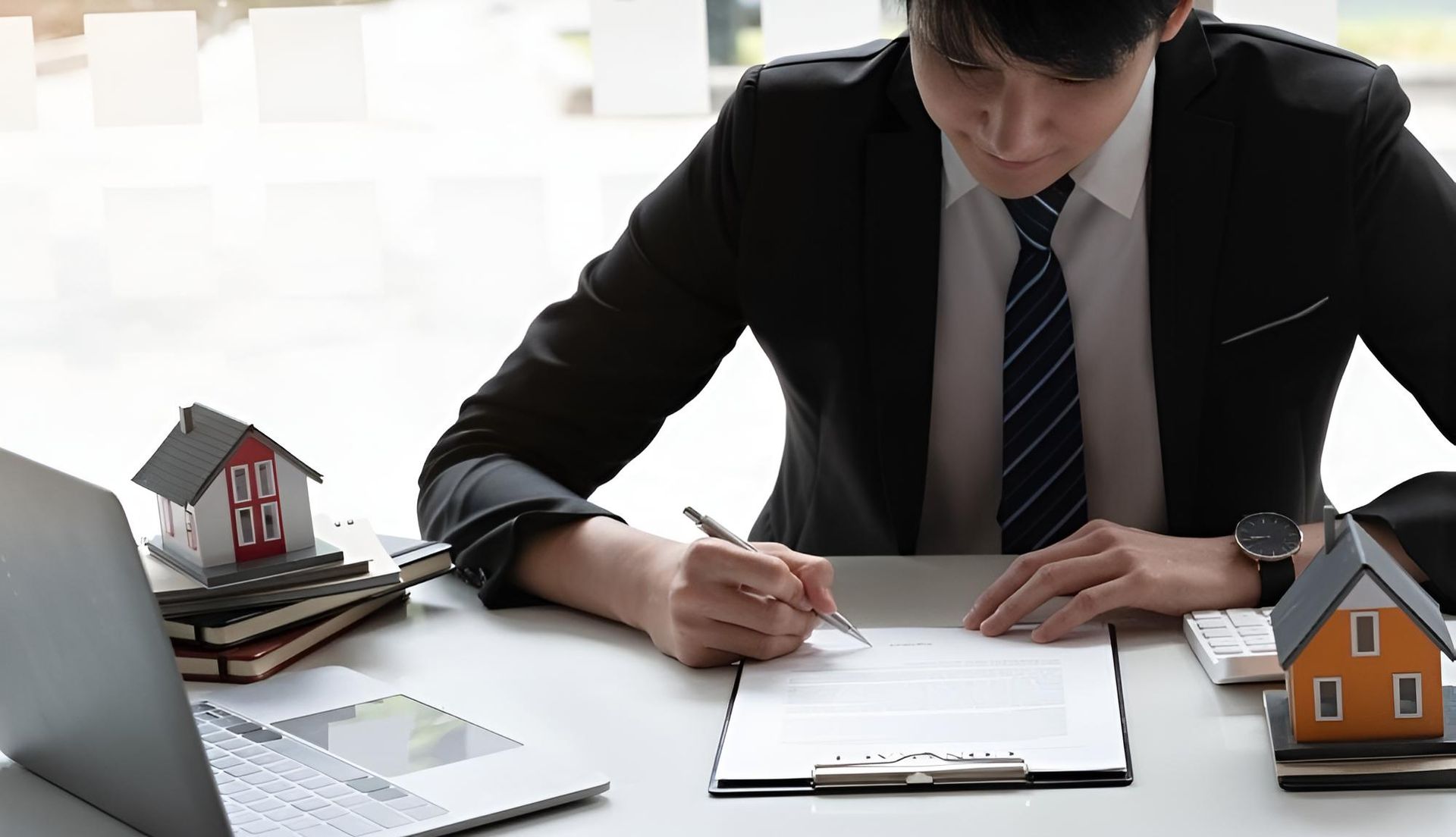 A Man in a Suit and Tie is Sitting at a Desk Signing a Document — Key2 Conveyancing In Forster, NSW