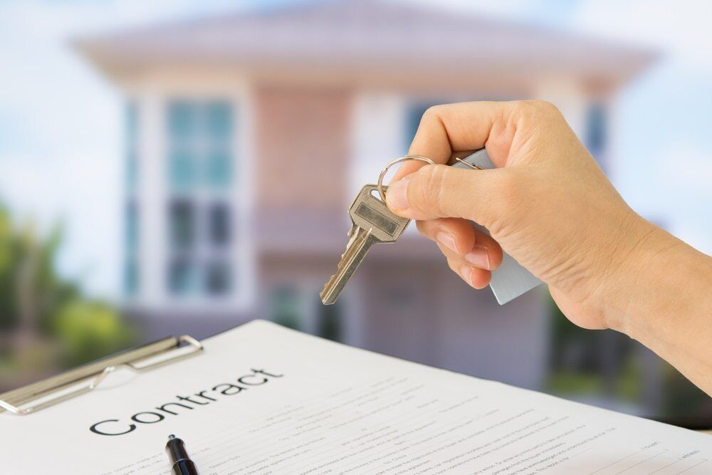 A Person is Holding a Key Over a Clipboard With a House in the Background — Key2 Conveyancing In Tea Gardens, NSW