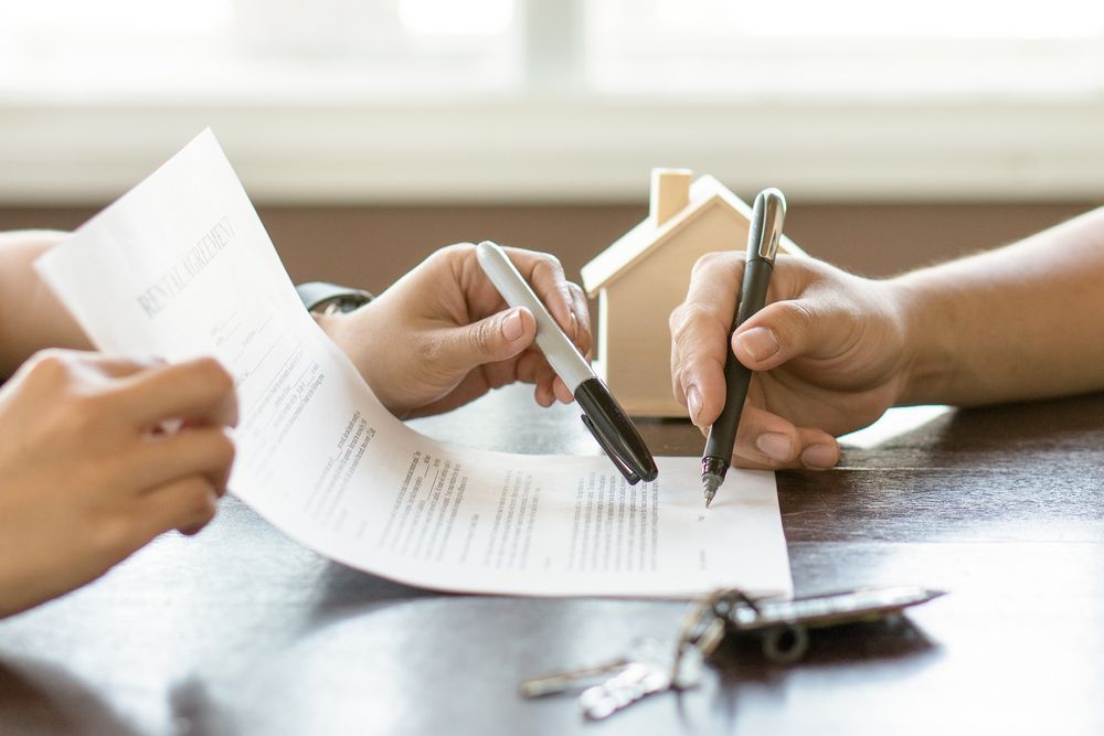 A Couple of People Are Sitting at a Table Signing a Document — Key2 Conveyancing In Mid North Coast, NSW