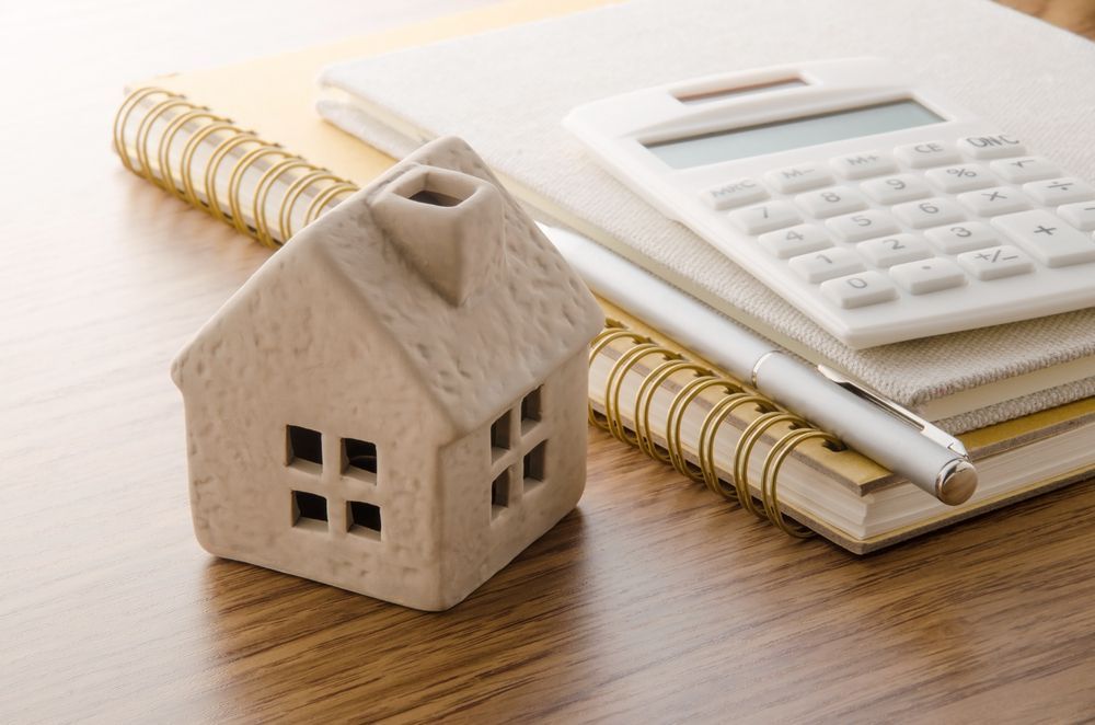 A Small House is Sitting on Top of a Notebook Next to a Calculator and Pen — Key2 Conveyancing In Diamond Beach, NSW