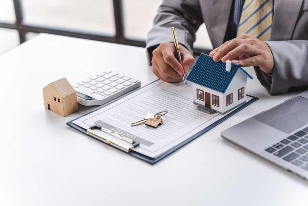 A Man is Sitting at a Desk With a Model House and Keys — Key2 Conveyancing In Hallidays Point, NSW