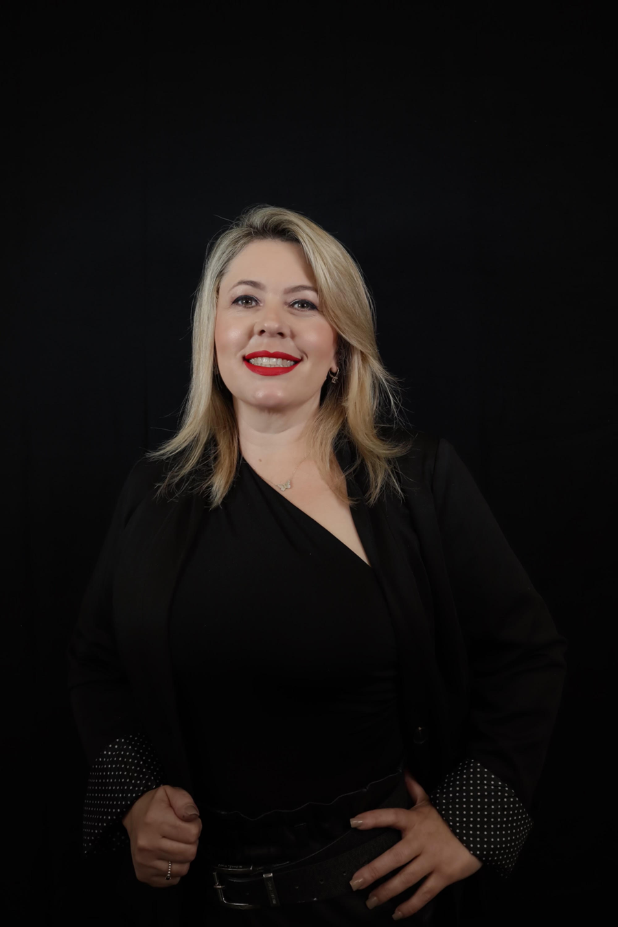 A woman in a black dress is standing in front of a black background.