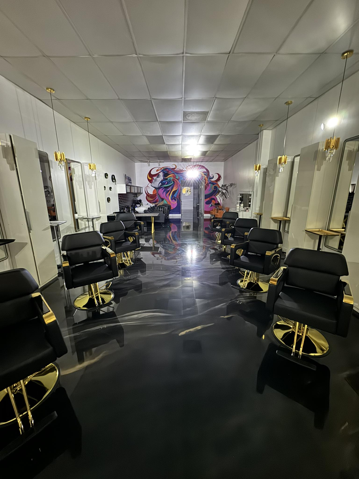 Hair salon interior with black and gold chairs, mirrors, and a colorful mural.