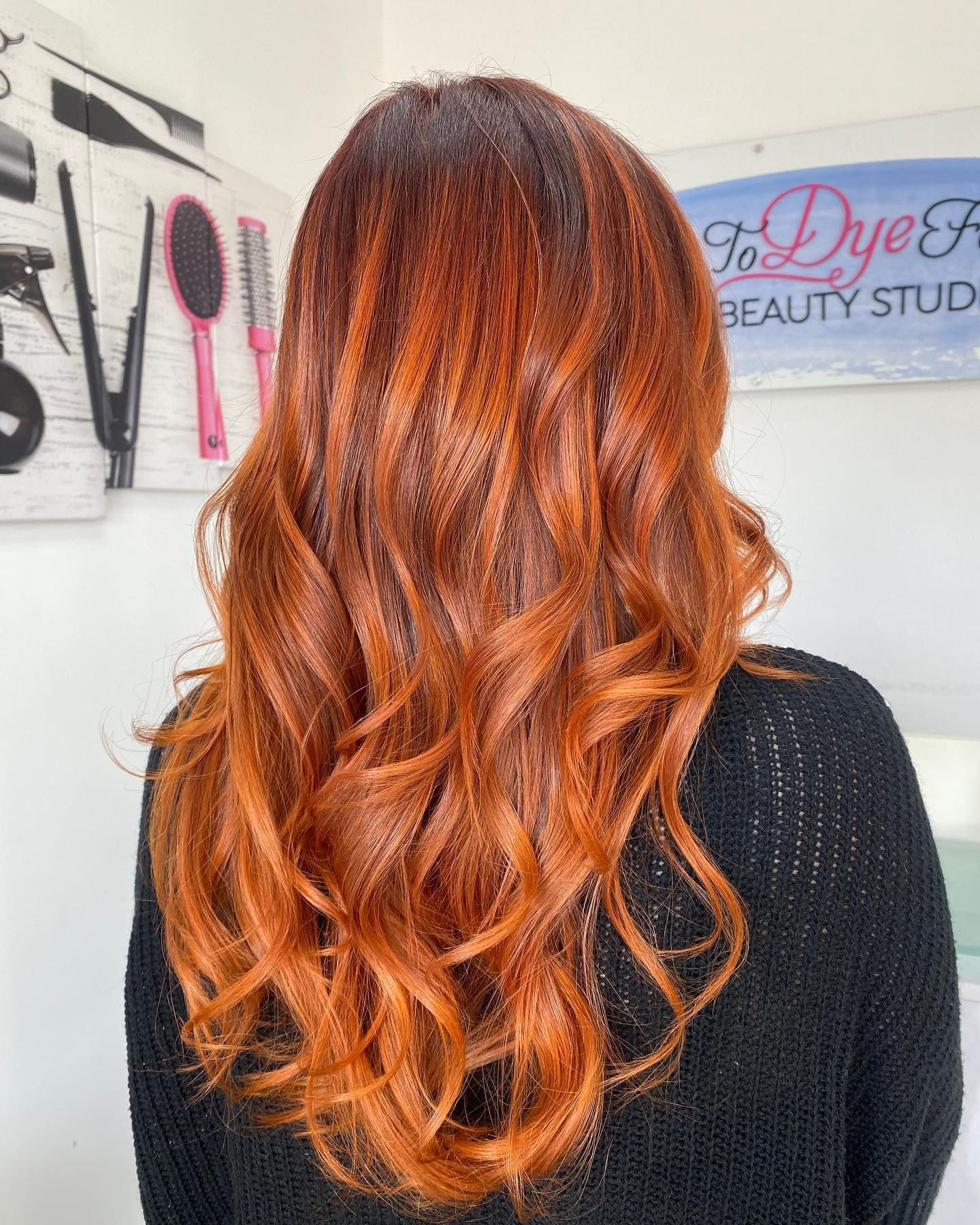 A woman with long red hair is wearing a black sweater.