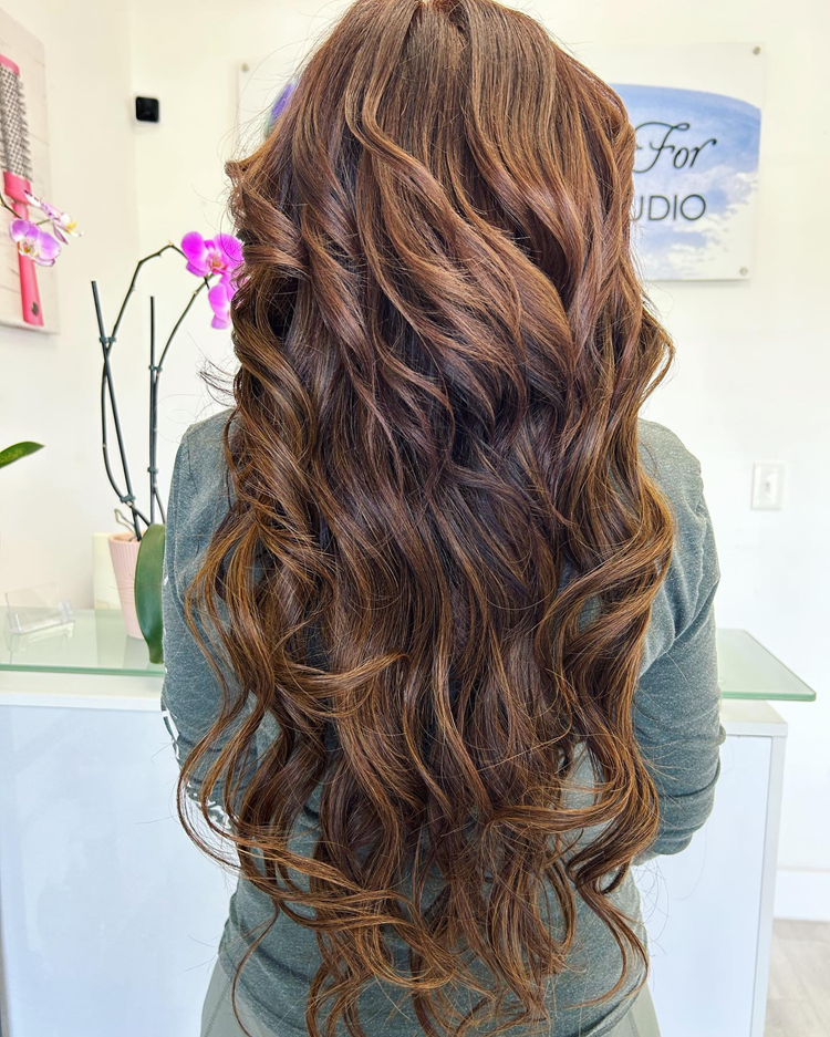 A woman with long brown curly hair is standing in a salon.