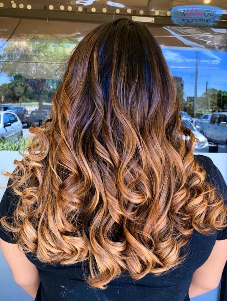 A woman with long curly hair is standing in front of a window.