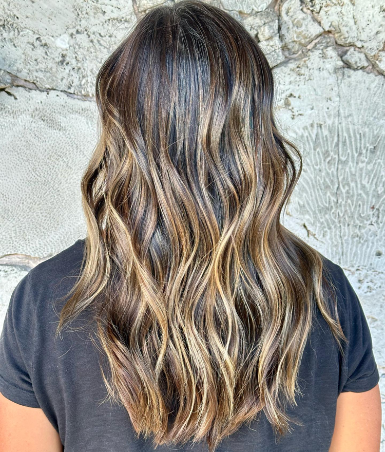 Woman with dark brown hair, balayage with blonde highlights, wavy hairstyle.