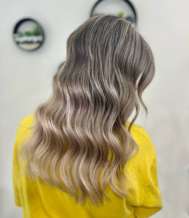 A woman with long wavy blonde hair is wearing a yellow shirt.