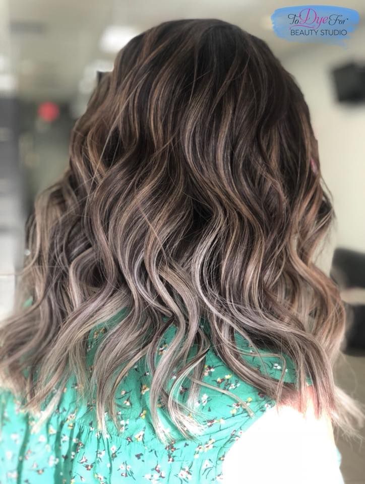 A woman with long wavy brown hair is wearing a green shirt.