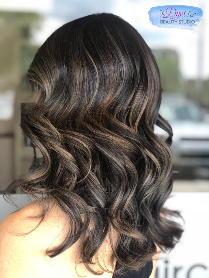 A woman with long dark hair is standing in front of a window.
