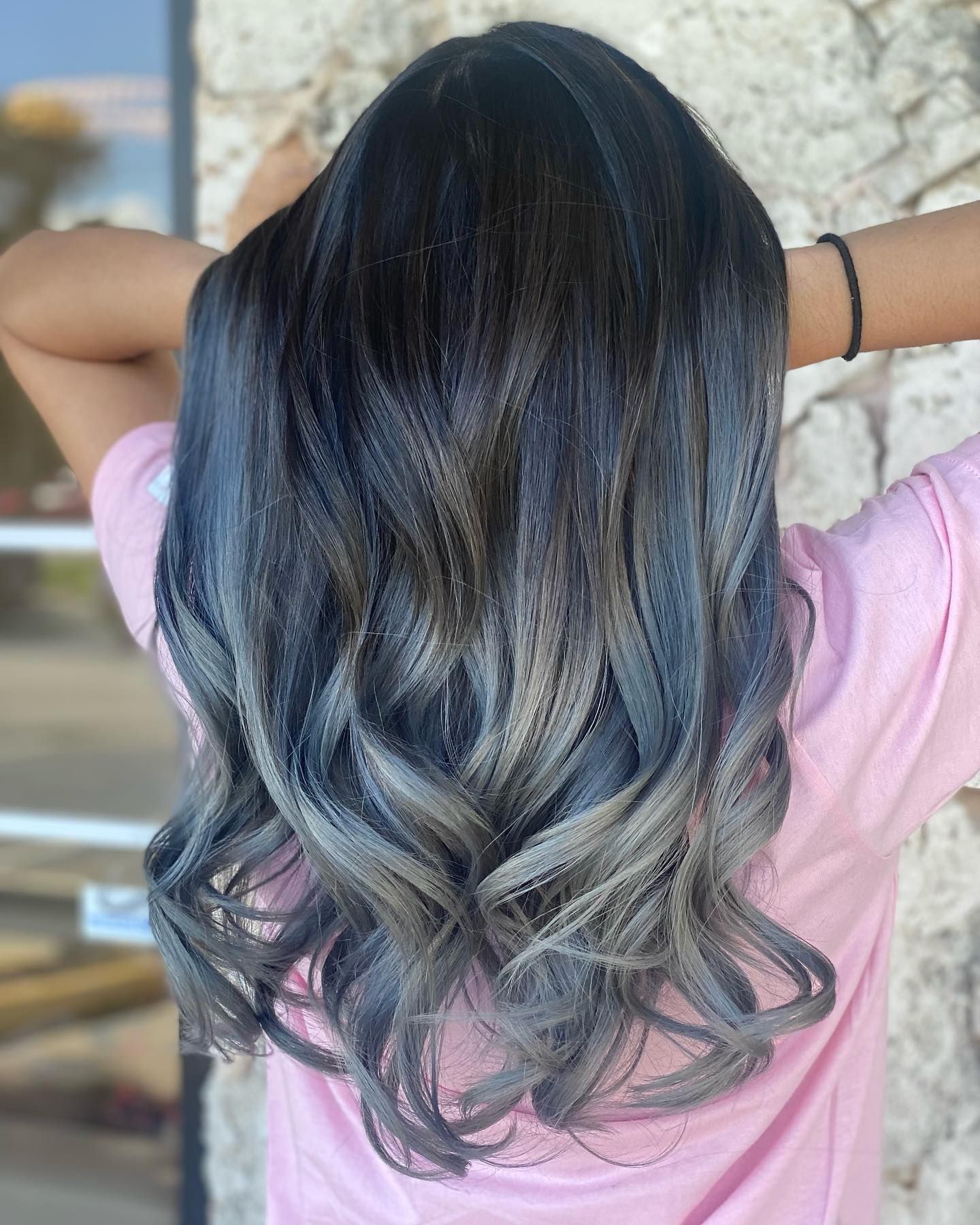 A woman with long black hair and gray highlights is wearing a pink shirt.